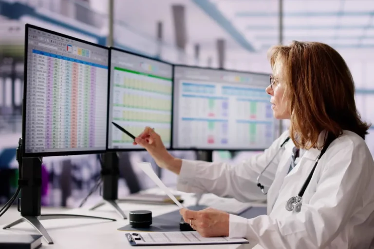 A woman in a lab coat examines data on a computer screen in a laboratory setting.